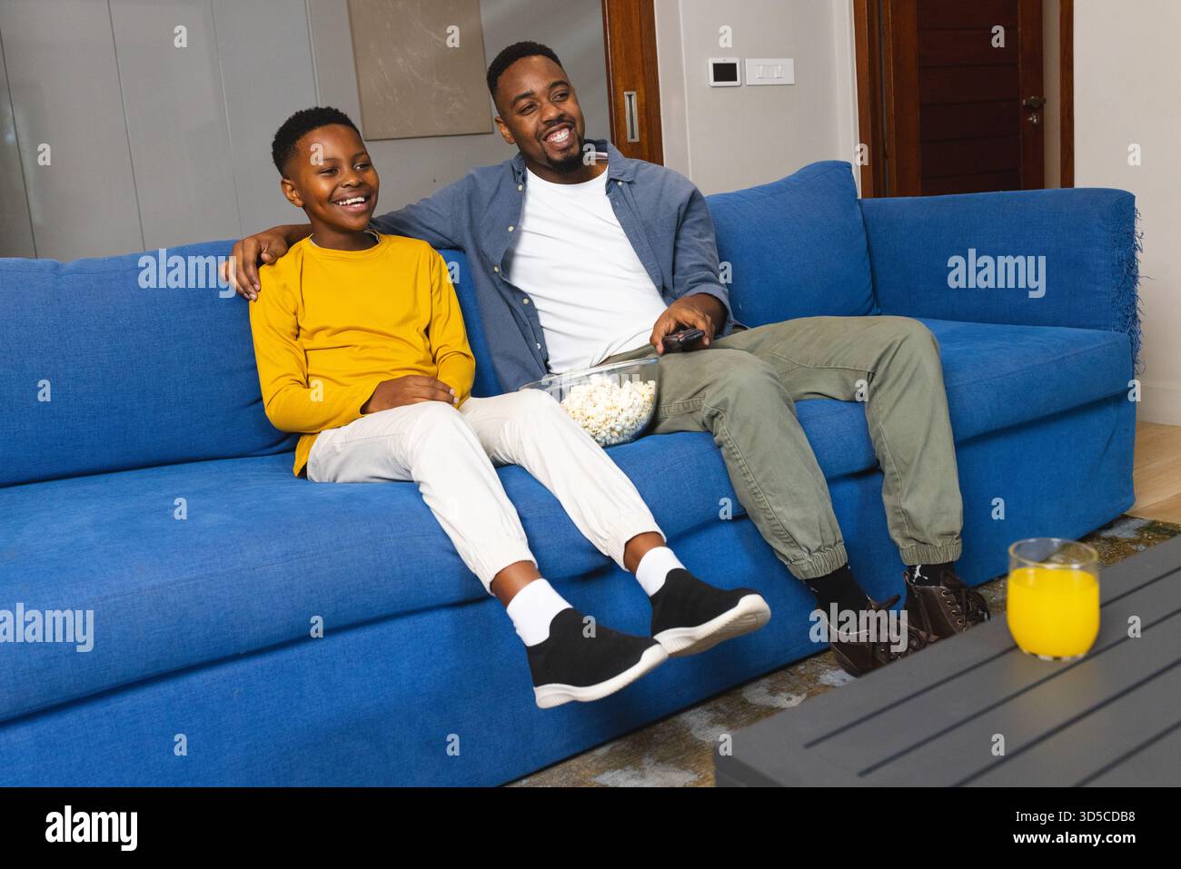 Padre e figlio si godevano il film sul divano, condividendo popcorn e risate a casa Foto Stock