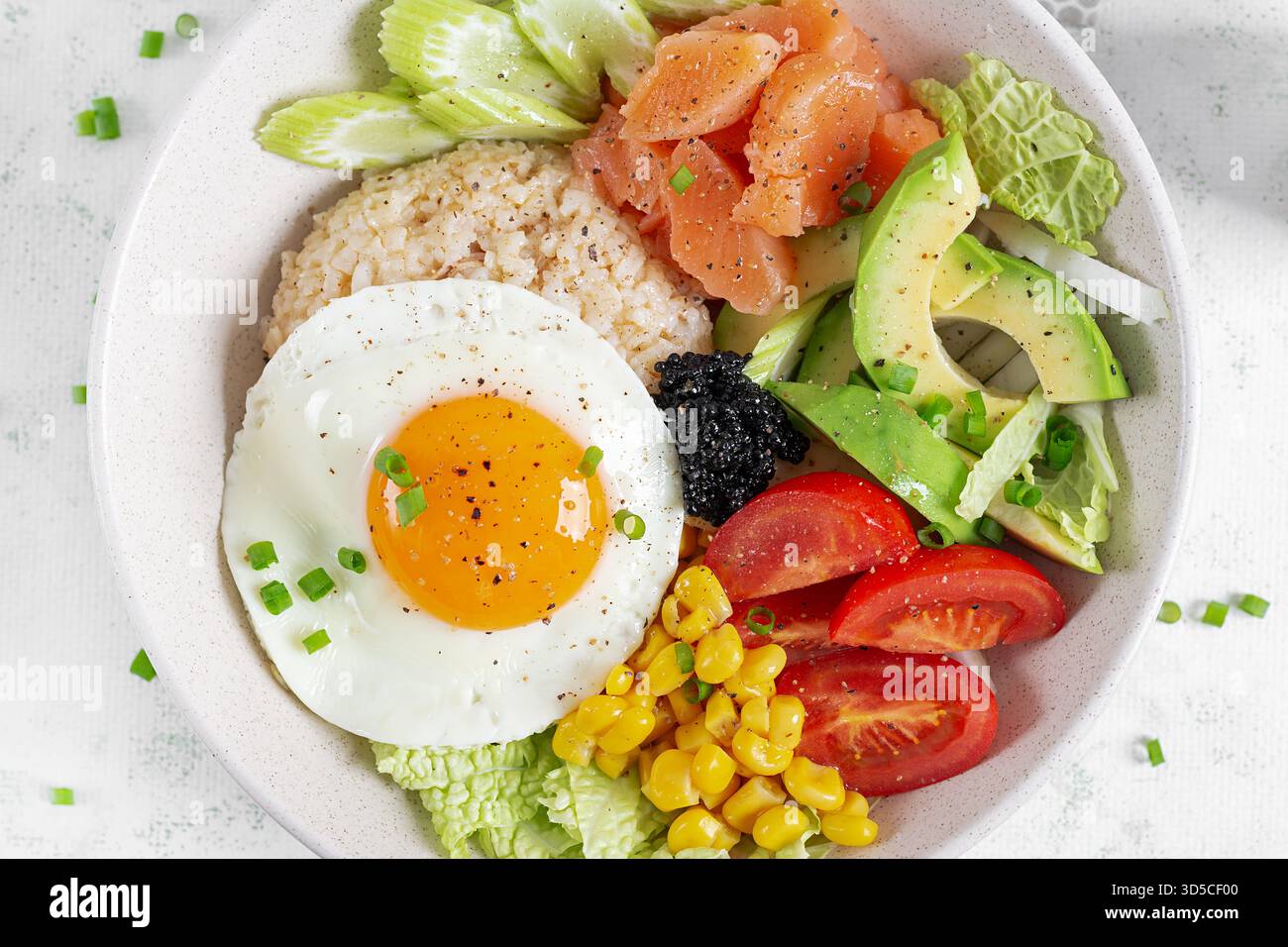Ciotola con ingredienti freschi come salmone, mais, avocado. pomodori e un uovo con il lato soleggiato su uno sfondo chiaro. Vista dall'alto Foto Stock