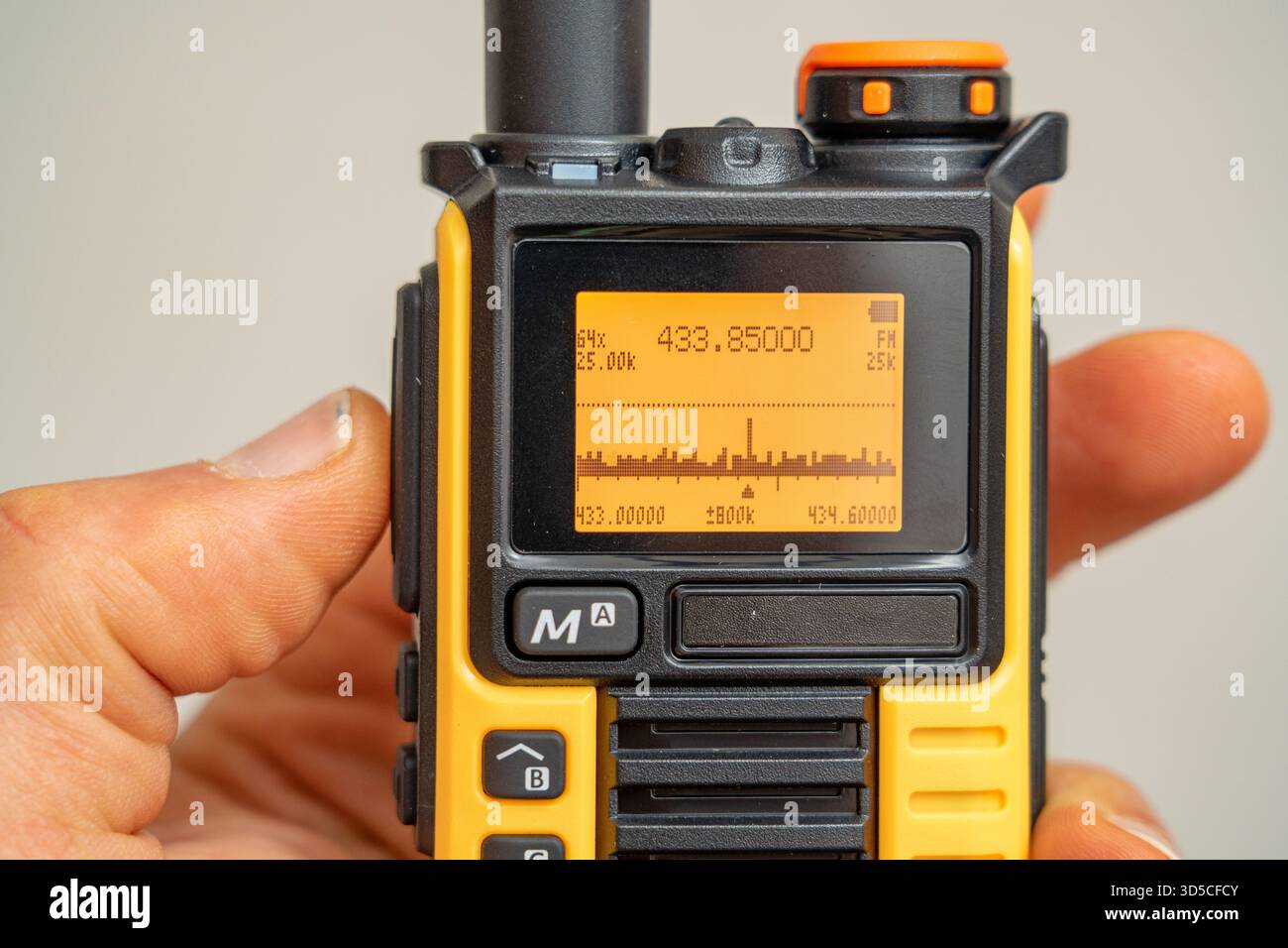 Radio walkie-talkie nera e grigia con display di frequenza e analizzatore di spettro, sicura in mano. Foto Stock