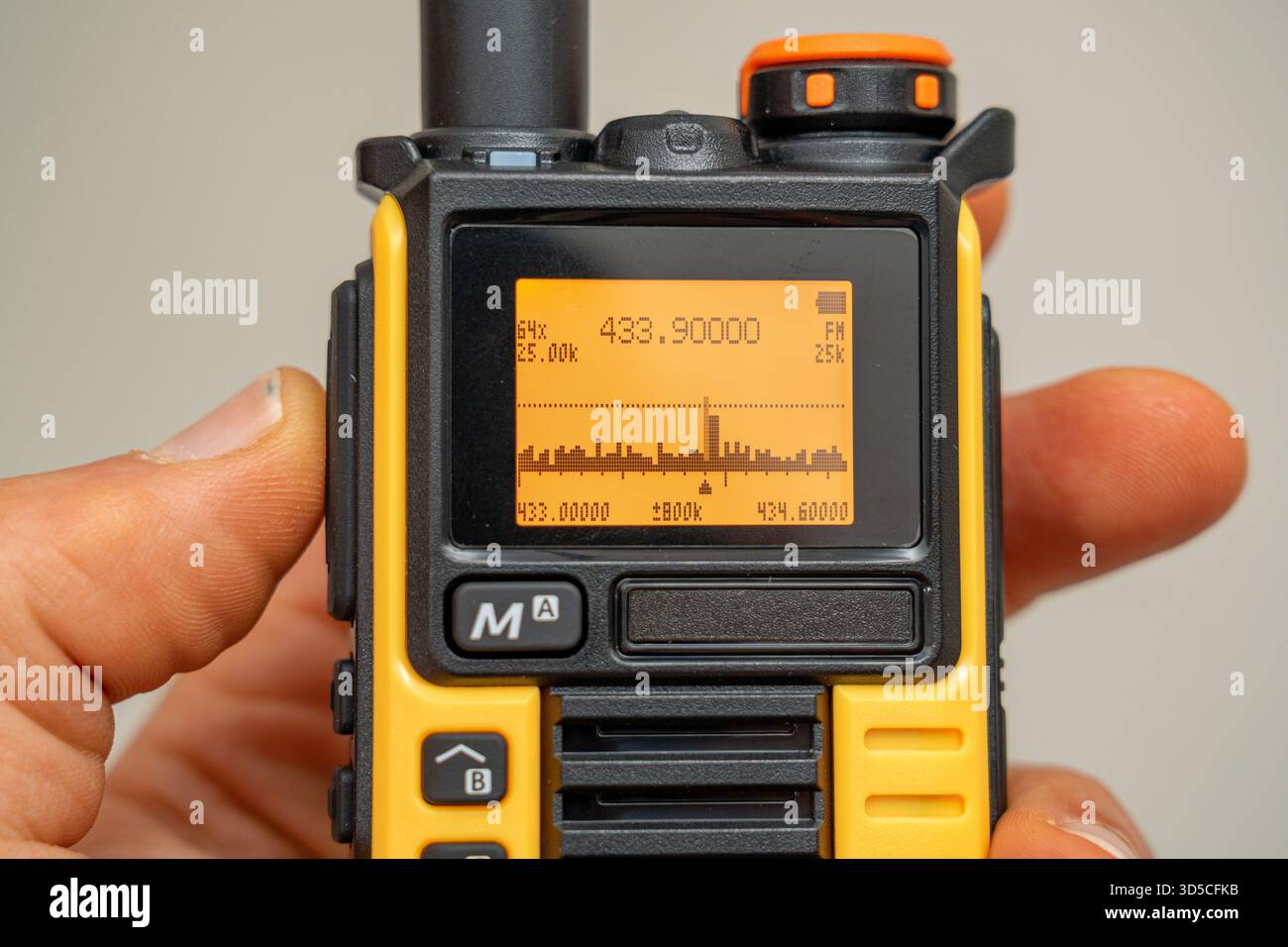 Radio walkie-talkie nera e grigia con display di frequenza e analizzatore di spettro, sicura in mano. Foto Stock