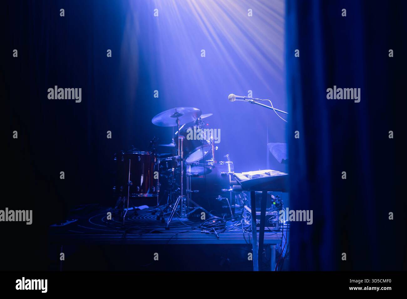 Palco vuoto con strumenti musicali e messa a fuoco selettiva sul microfono sotto l'illuminazione blu del concerto. La scena cattura l'atmosfera di soundcheck, concerto p Foto Stock