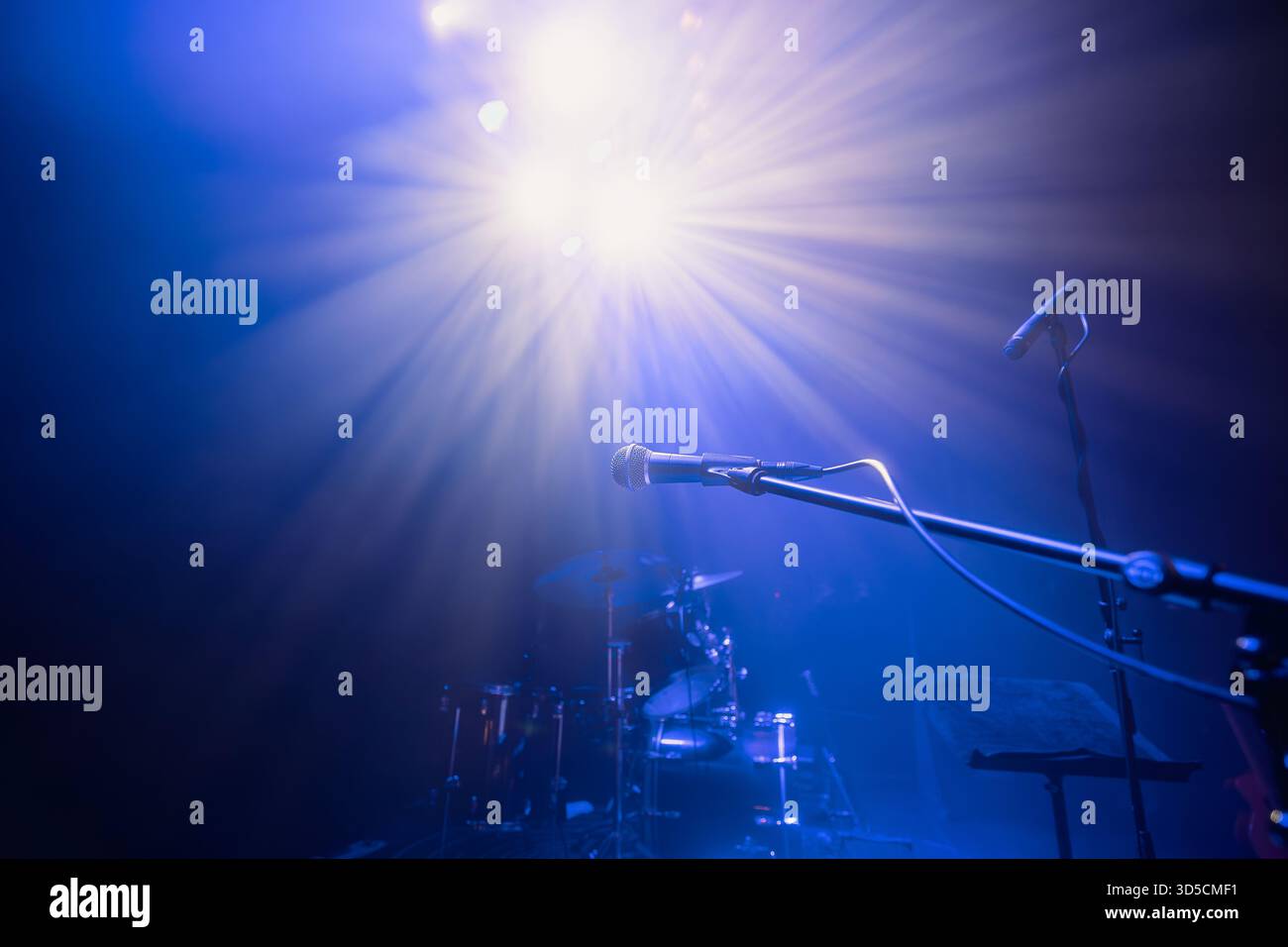 Palco vuoto con strumenti musicali e messa a fuoco selettiva sul microfono sotto l'illuminazione blu del concerto. La scena cattura l'atmosfera di soundcheck, concerto p Foto Stock