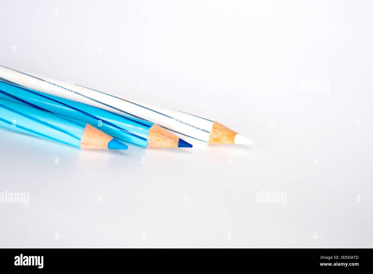 Tre matite colorate a strisce, con sfumature di blu e bianco, poggiano diagonalmente su uno sfondo bianco. L'attenzione è concentrata sulle punte affilate. Foto Stock