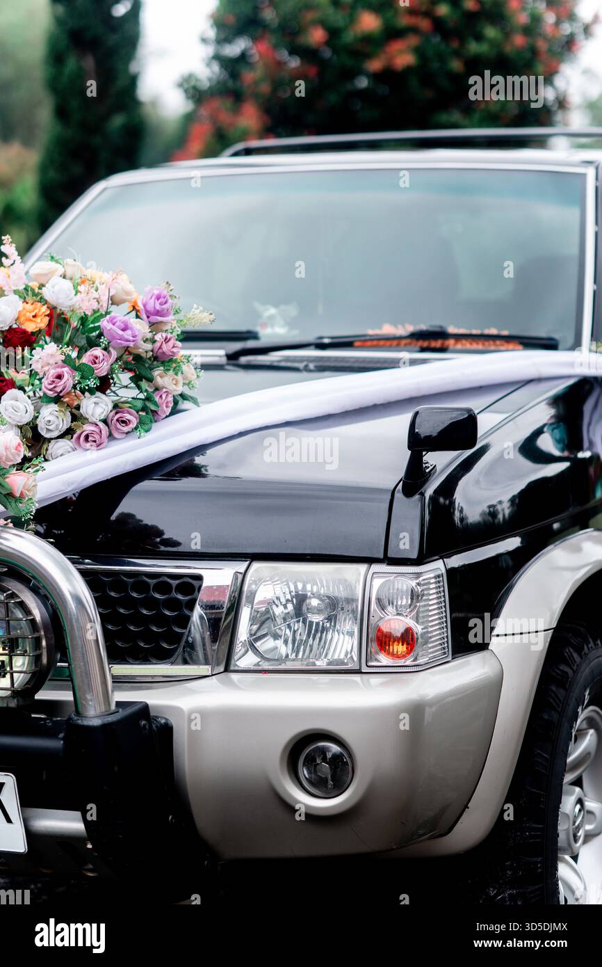 Vista ravvicinata del cappuccio di un SUV nero decorato per un matrimonio con un bouquet floreale colorato e un nastro in raso bianco. Foto Stock