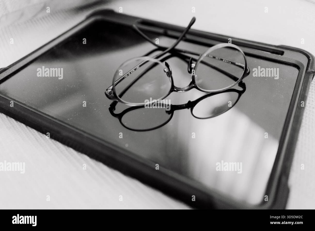 Un paio di occhiali da vista rotondi con montature dorate su una superficie in vetro riflettente, illuminati da luce soffusa, che evocano studio, lettura o atmosfera premurosa Foto Stock