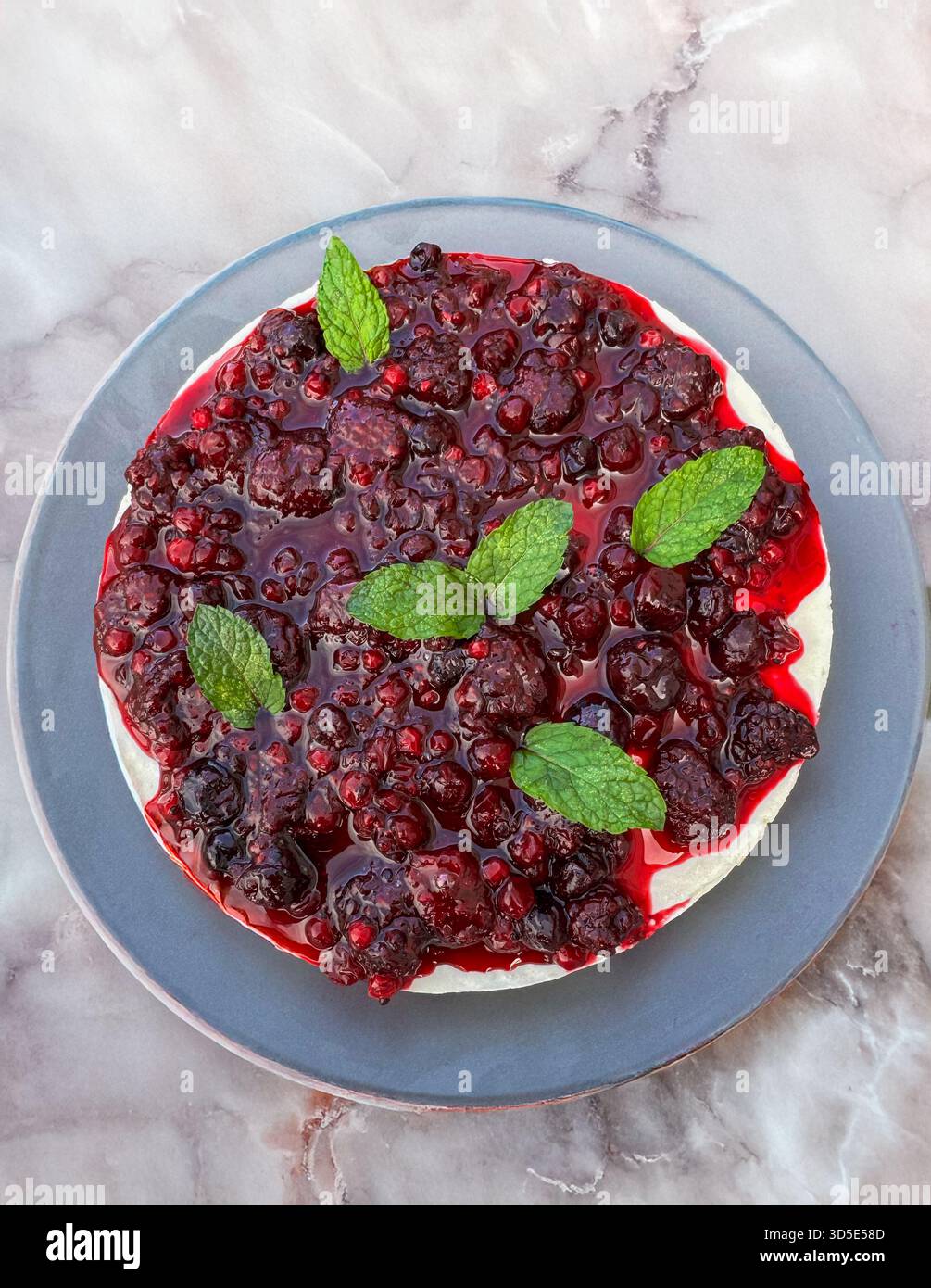 Vista dall'alto della cheesecake cremosa con frutti di bosco misti lucidi e foglie di menta. Foto Stock
