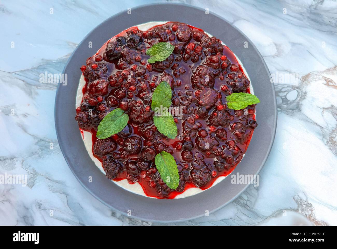Vista dall'alto della cheesecake cremosa con frutti di bosco misti lucidi e foglie di menta. Foto Stock