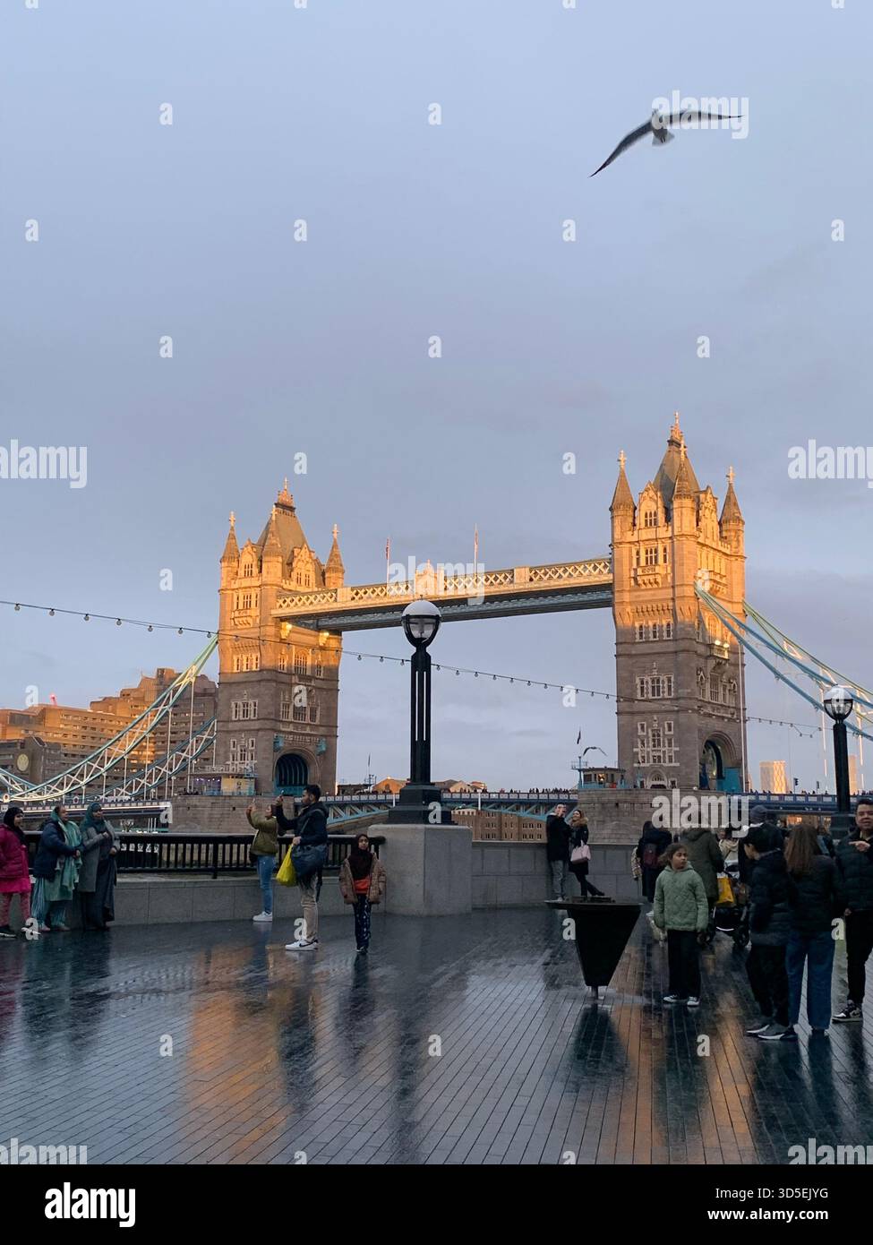 L'iconico Tower Bridge illuminato dalla calda luce serale con i pedoni che camminano sul ponte. Famoso punto di riferimento di Londra e attrazione turistica - Immagine stock catturata con smartphone
