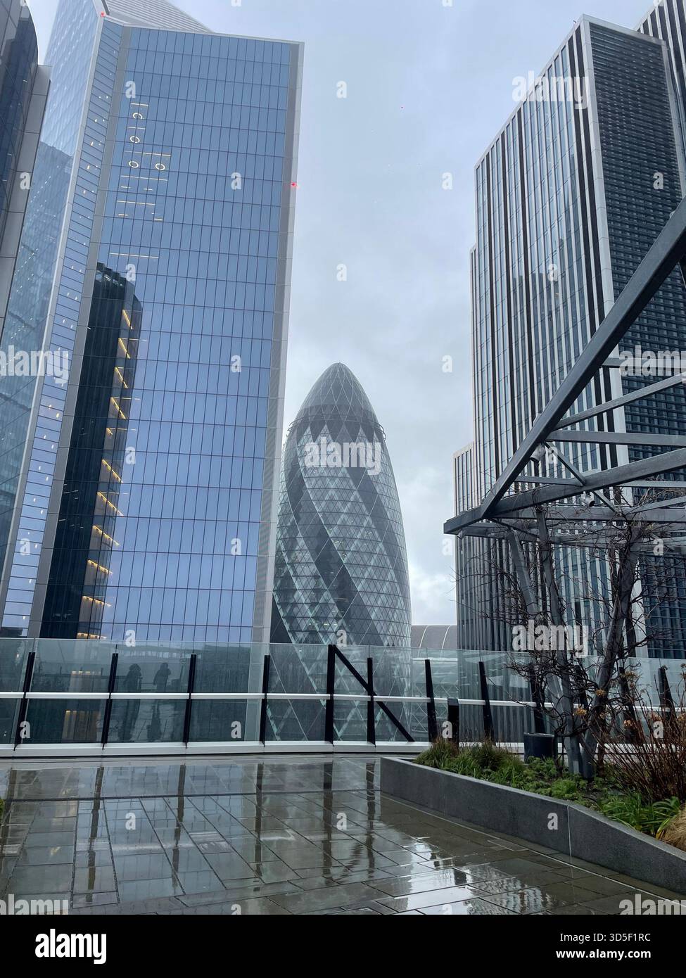 Architettura contemporanea nel quartiere finanziario della City of London con moderni grattacieli di vetro e l'iconico edificio Gherkin in una giornata di pioggia. Foto Stock