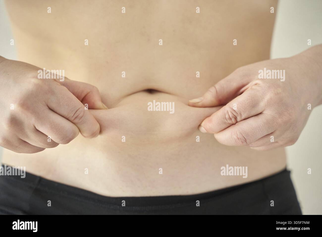 Adulto caucasico che manifesta un pizzico della pelle addominale per la valutazione del grasso corporeo Foto Stock