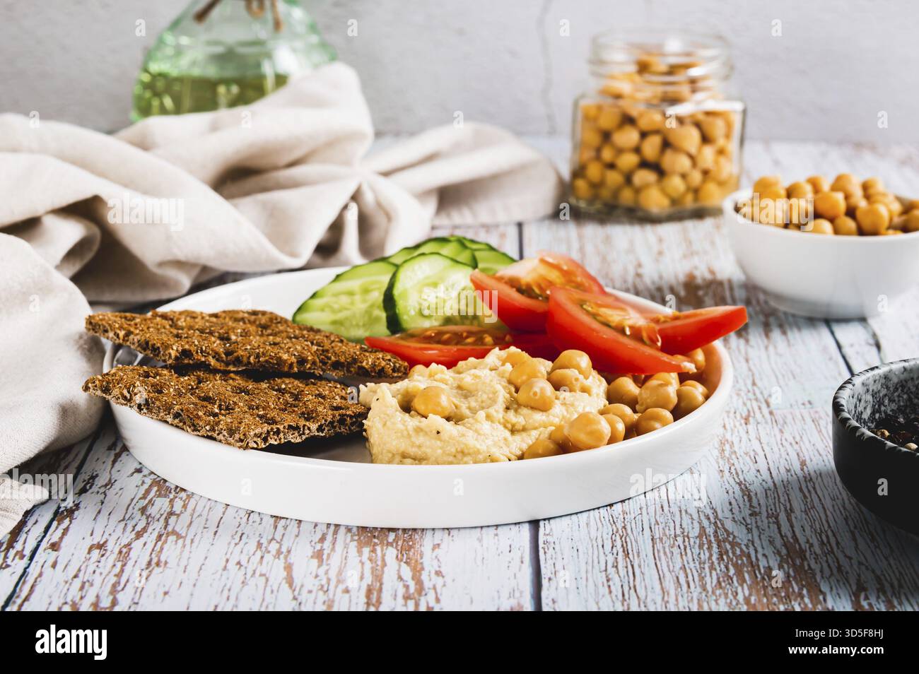 Hummus, ceci, pomodoro, cetriolo, cracker di grano su un piatto sul tavolo Foto Stock