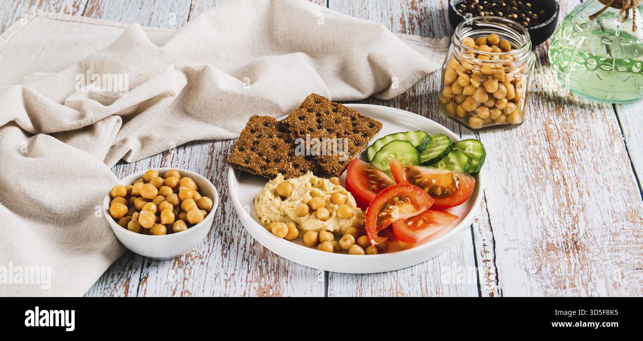 Hummus, ceci, pomodori, cetrioli, cracker di grano su un piatto sul banner del tavolo Foto Stock