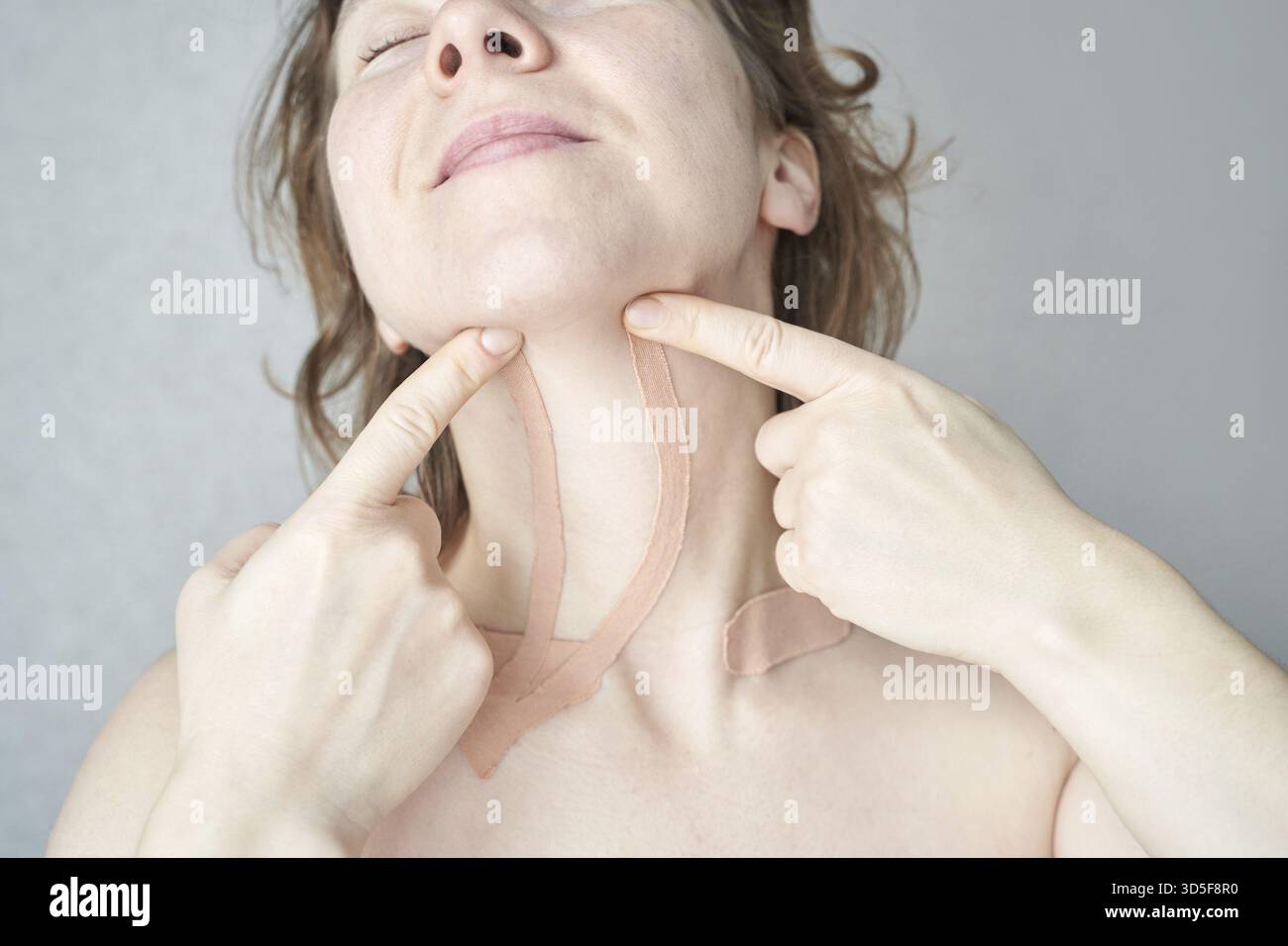 Donna caucasica adulta che utilizza la tecnica del nastro per rassodare la pelle e anti-invecchiamento in un ritratto in primo piano Foto Stock