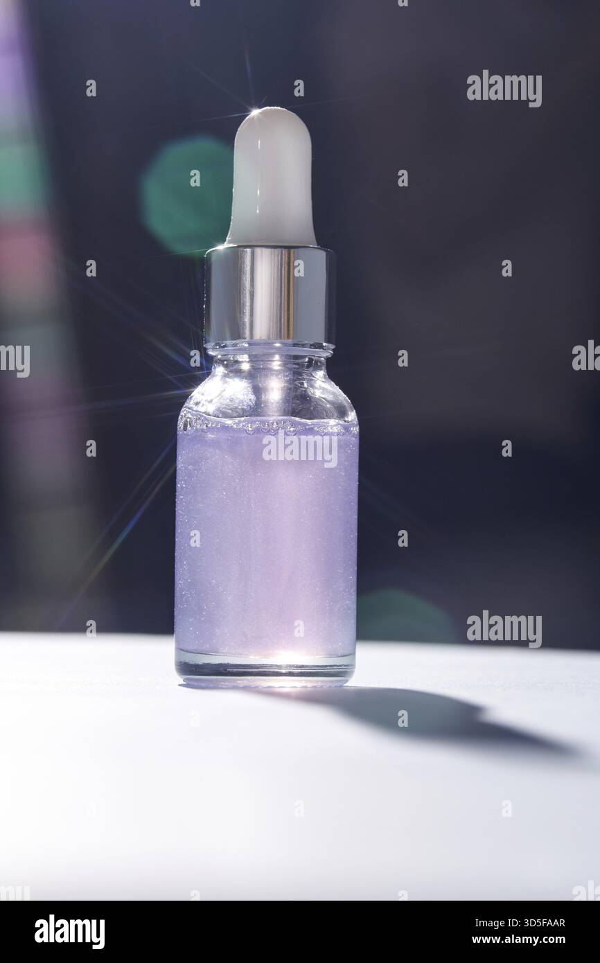 Flacone luminoso di siero liquido viola con coperchio contagocce ed effetti di luce bokeh alla luce del sole Foto Stock