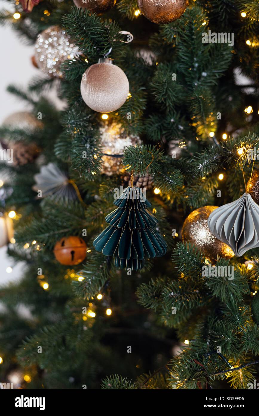 Decorazioni moderne sull'albero di Natale con decorazioni in carta a nido d'ape, baule in velluto e calde luci fiabesche sui rami verdi. Foto Stock