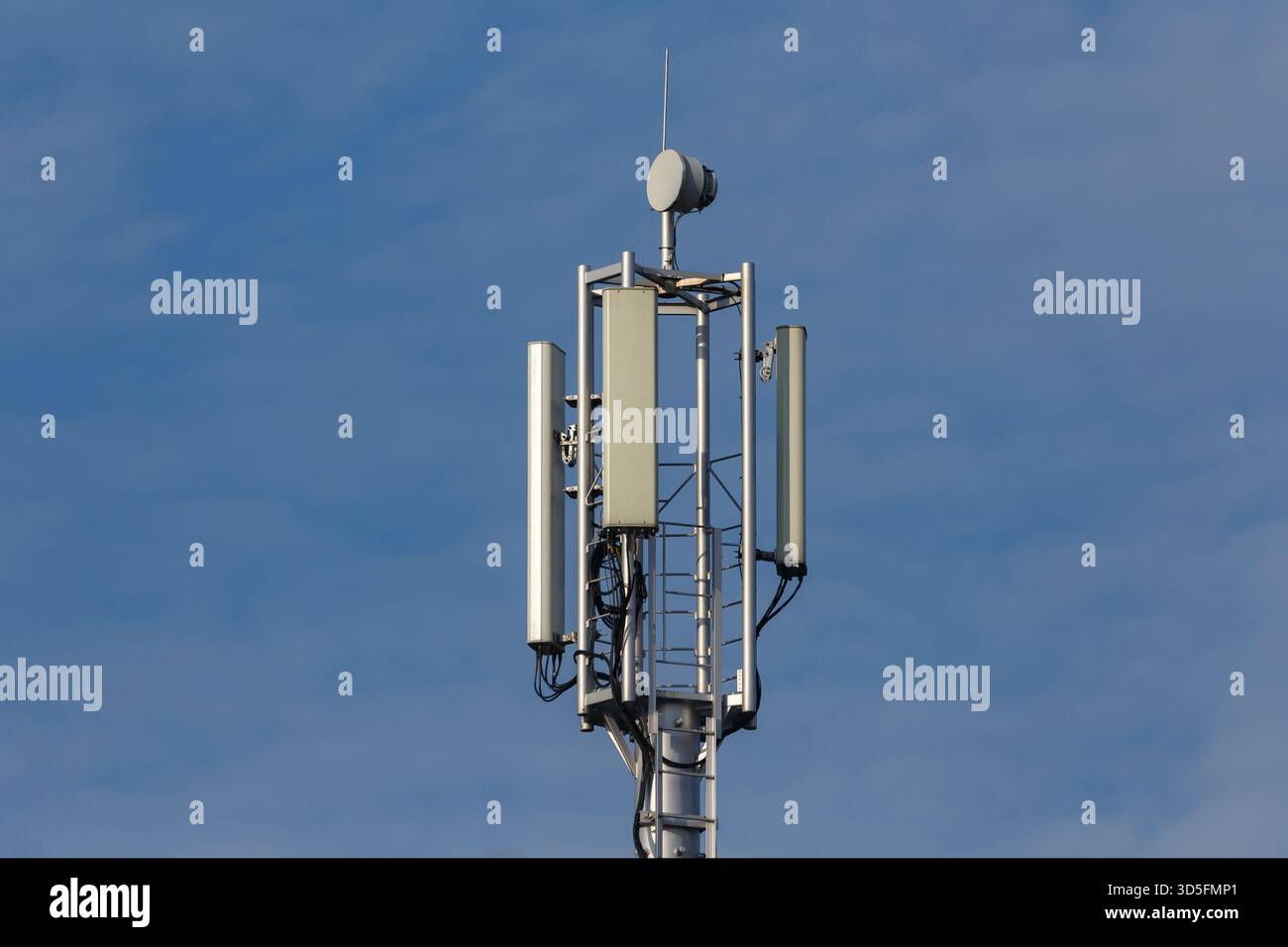 Una torre di telecomunicazioni per telefoni cellulari con pannelli di antenna e un'antenna parabolica contro un cielo blu Foto Stock