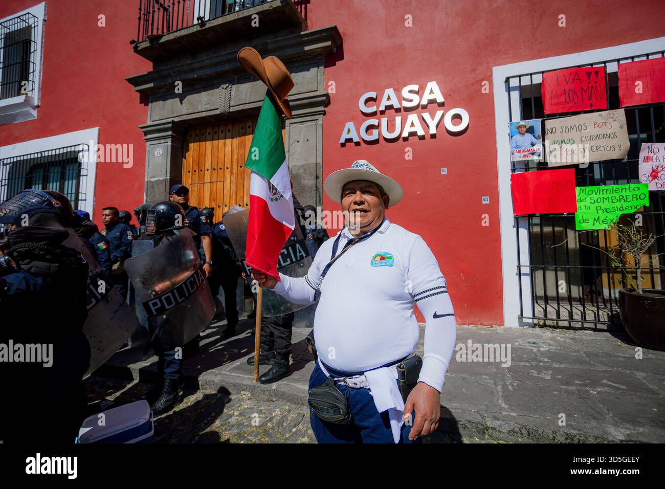 Un manifestante maschile che detiene la bandiera messicana sfida la polizia antisommossa durante la marcia contro il governo Morena a Puebla. Foto Stock