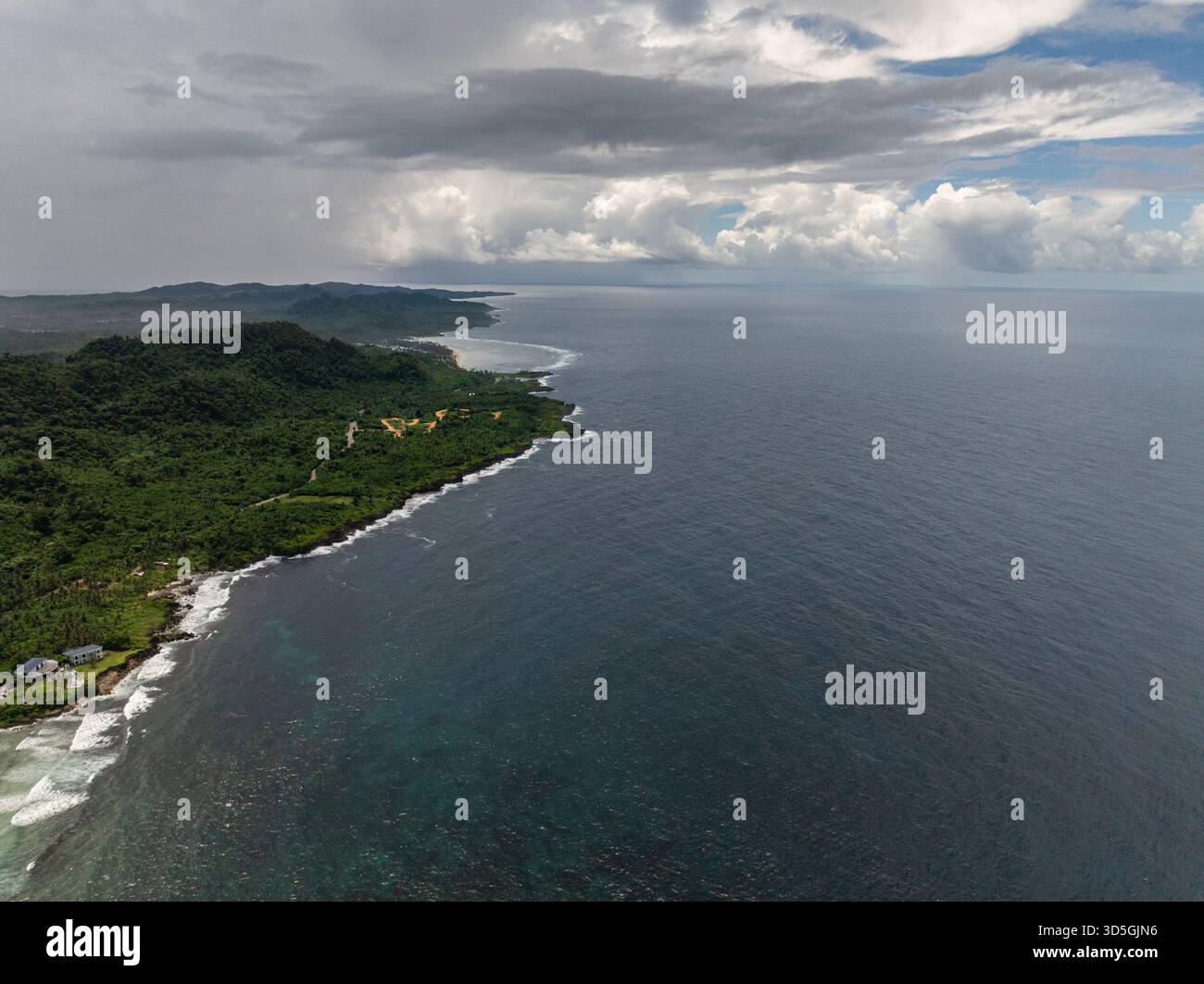 Verdi colline si estendono lungo la costa sotto un cielo nuvoloso con onde che si infrangono sulla riva. Siargao, Filippine. Foto Stock