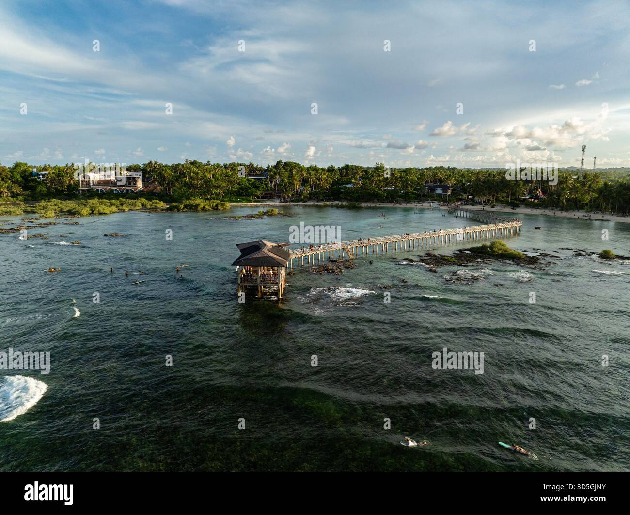 Molo in legno che si estende nell'oceano con surfisti che cavalcano le onde vicino alla riva. Siargao, Filippine. Foto Stock