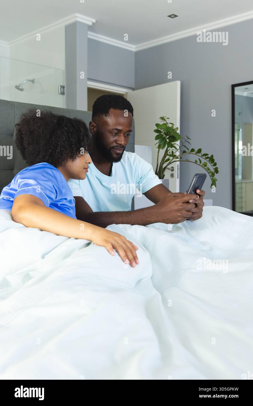 Coppia che si rilassa a letto, guarda lo smartphone insieme e goditi il tempo libero a casa Foto Stock