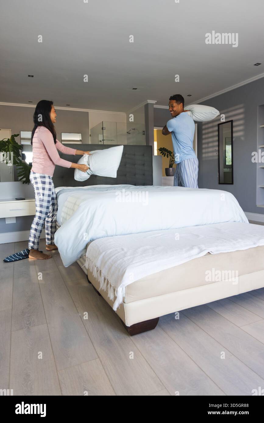 Coppia giocherellando con i cuscini in camera da letto, godendosi la mattinata insieme Foto Stock