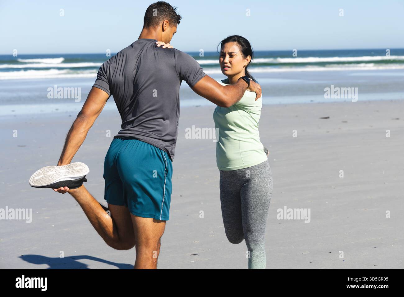 Coppia che si allunga insieme sulla spiaggia, godendosi l'esercizio mattutino vicino all'oceano Foto Stock
