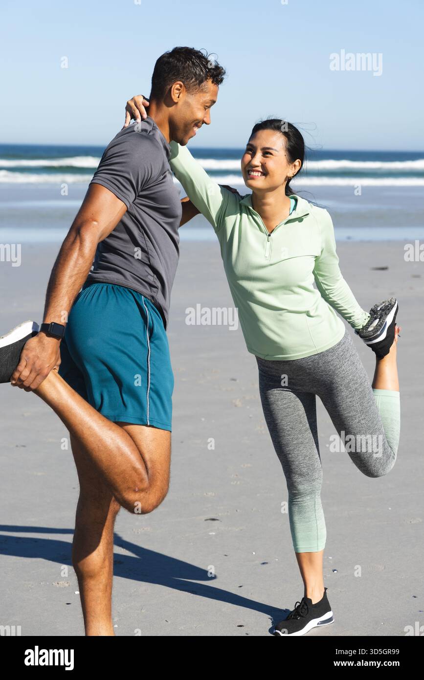 Coppia che si allunga sulla spiaggia, sorride e si diverte ad allenarsi al mattino insieme Foto Stock