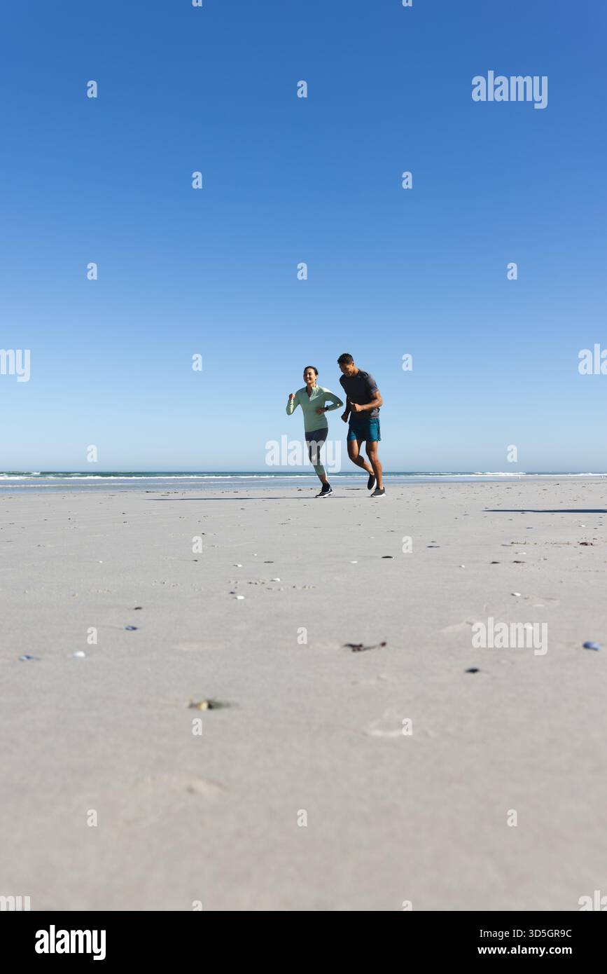 Coppia che fa jogging sulla spiaggia, si fa esercizio mattutino sotto il cielo azzurro e si copia spazio Foto Stock