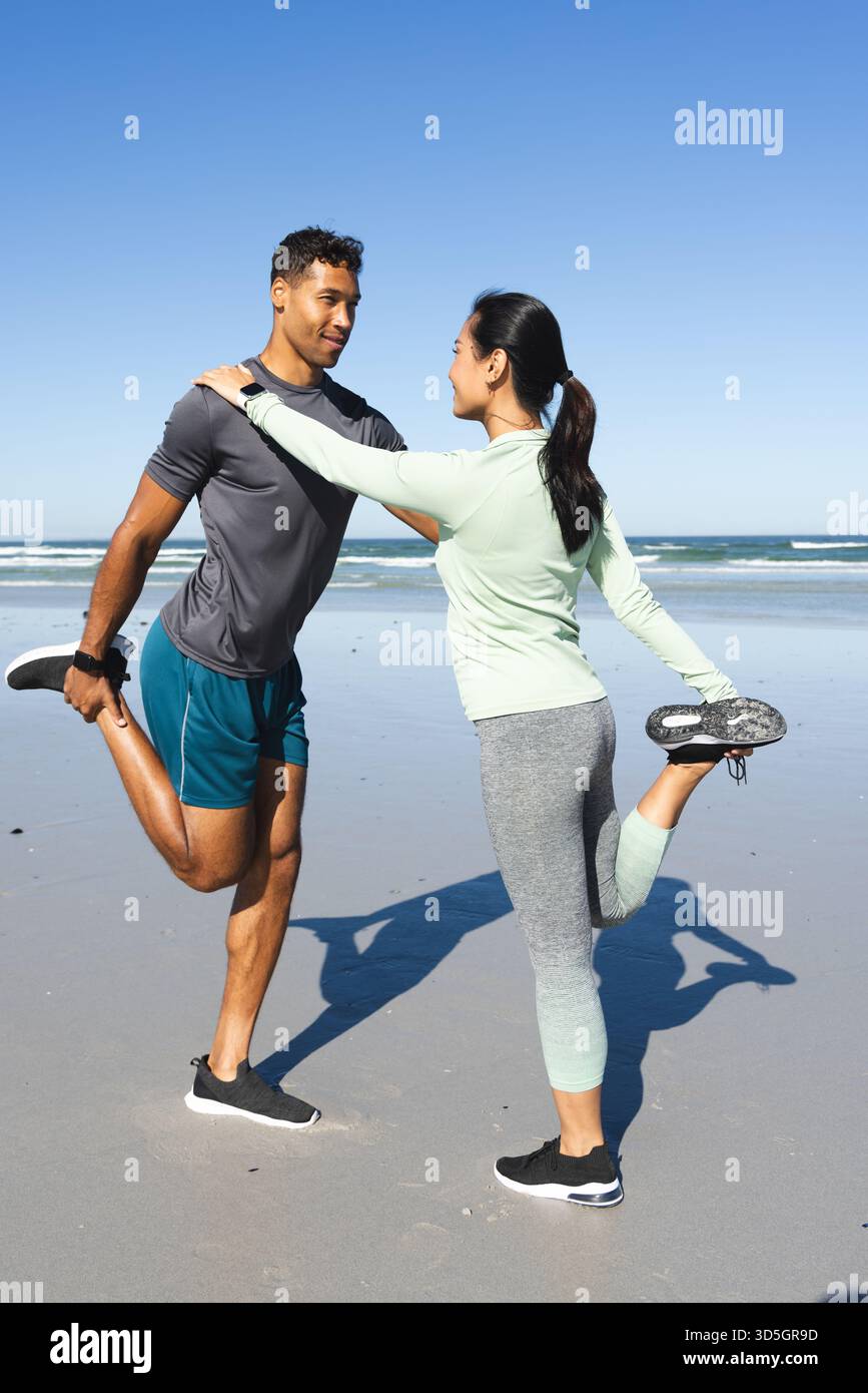 Coppia che si allunga insieme sulla spiaggia, godendosi l'esercizio mattutino vicino all'oceano Foto Stock