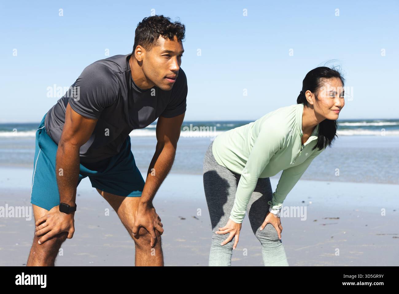 Coppia in forma che si prende una pausa dal jogging sulla spiaggia, godendosi la fresca brezza dell'oceano Foto Stock