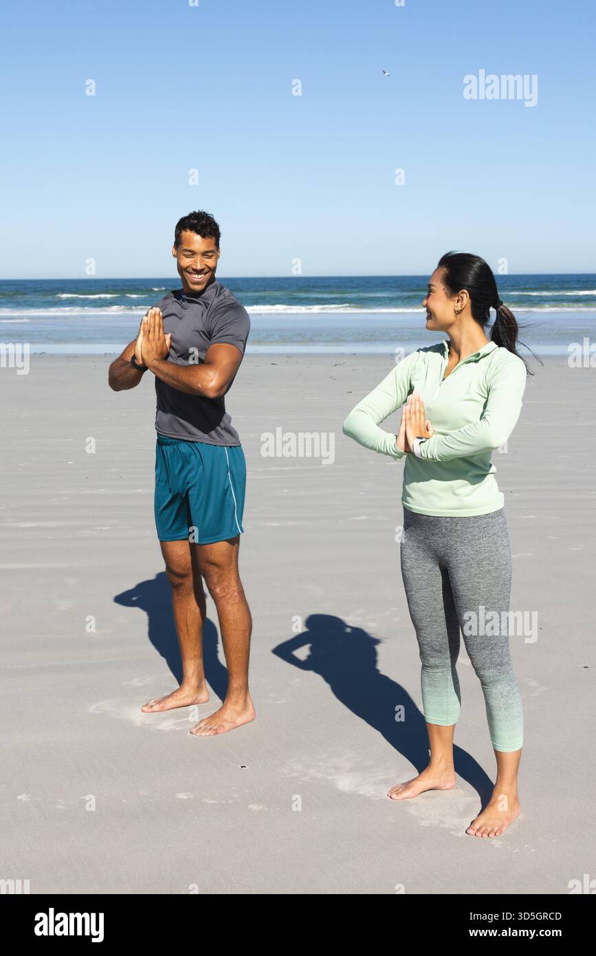 Coppia che pratica yoga sulla spiaggia, sorridendo e godendo insieme una giornata di sole Foto Stock