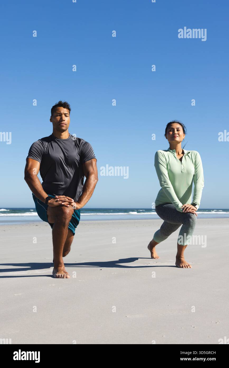 Coppia che si fa esercizio sulla spiaggia, facendo affondi sotto il cielo azzurro Foto Stock