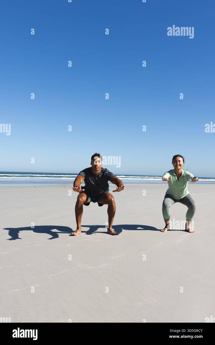 Coppia che si fa esercizio sulla spiaggia, esegue squat insieme sotto il cielo azzurro, copia lo spazio Foto Stock