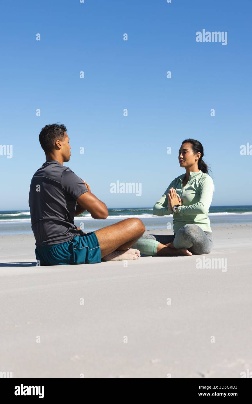 Coppia che pratica yoga sulla spiaggia, seduti a gambe incrociate e meditando insieme Foto Stock