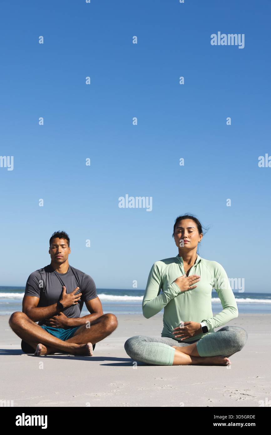Coppie che meditano sulla spiaggia, esercitano consapevolezza e relax sotto il cielo limpido, copiano lo spazio Foto Stock