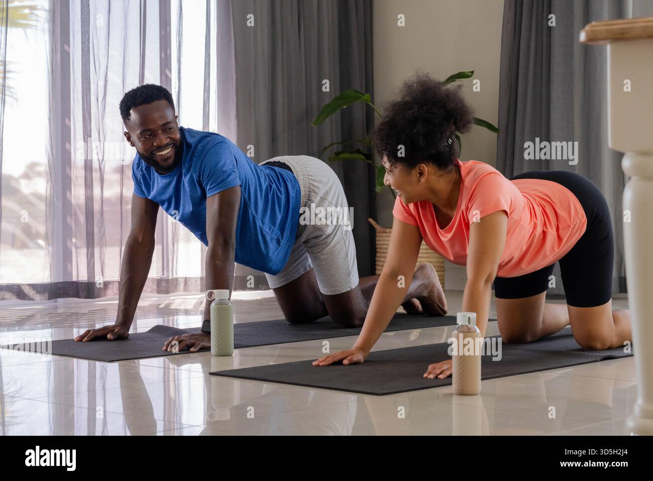 Coppia afroamericana che fa yoga insieme sui tappetini a casa, sorridente e rilassata Foto Stock