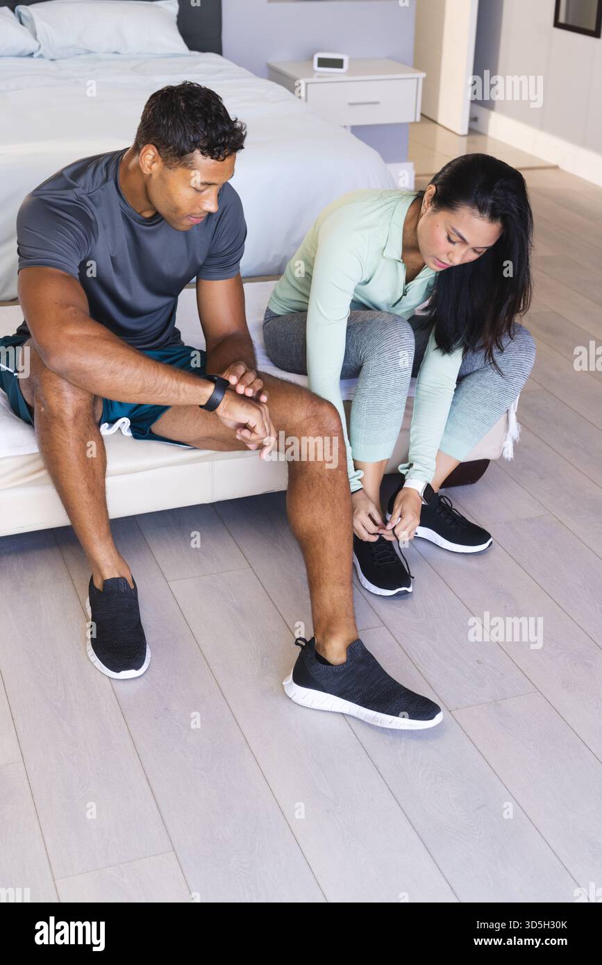 Coppia che si prepara per l'allenamento mattutino, legando le scarpe sul letto in camera da letto Foto Stock