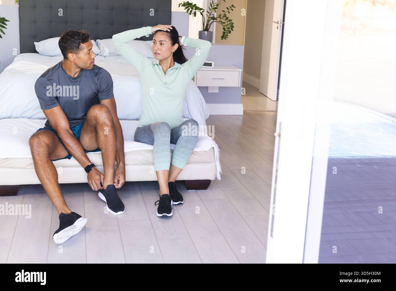 Coppia che si prepara per l'allenamento mattutino a casa, seduto sul letto legando scarpe Foto Stock
