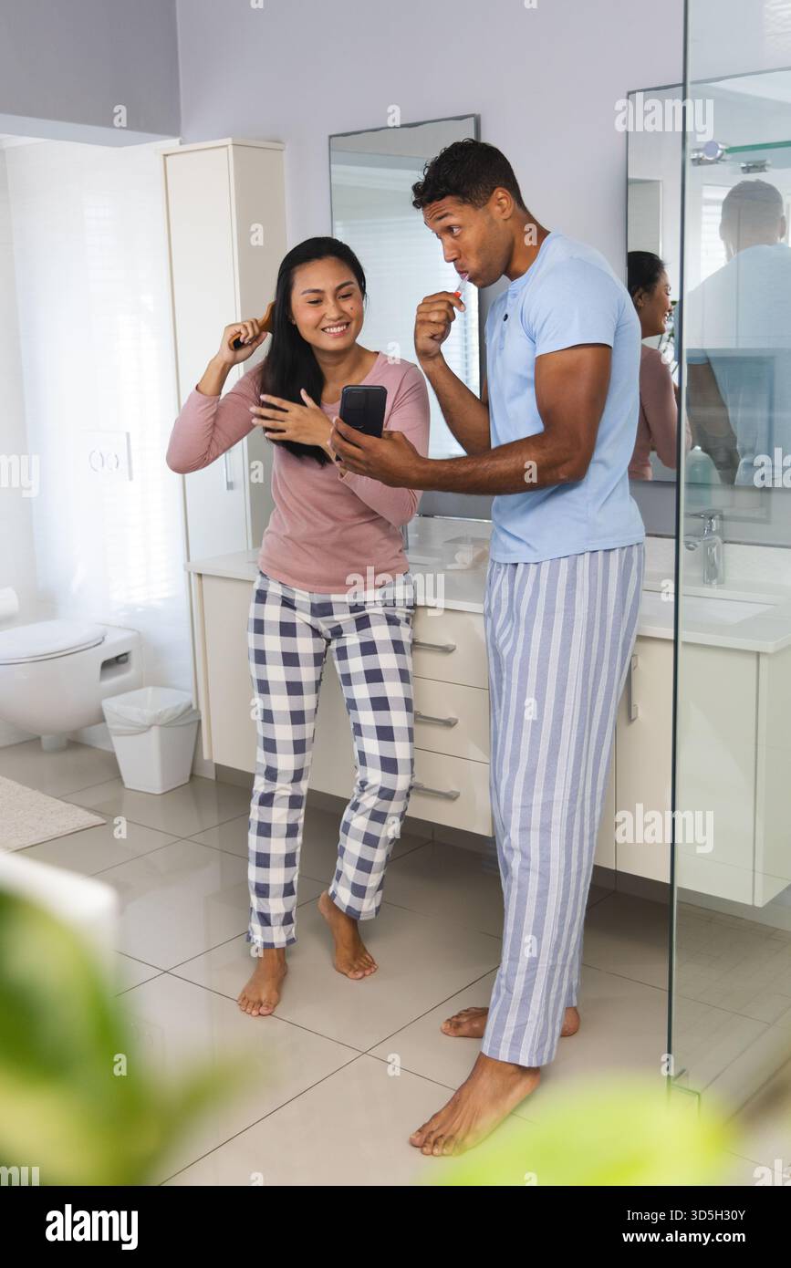 Coppia in bagno a lavarsi i denti e a usare lo smartphone, godendosi la routine mattutina Foto Stock