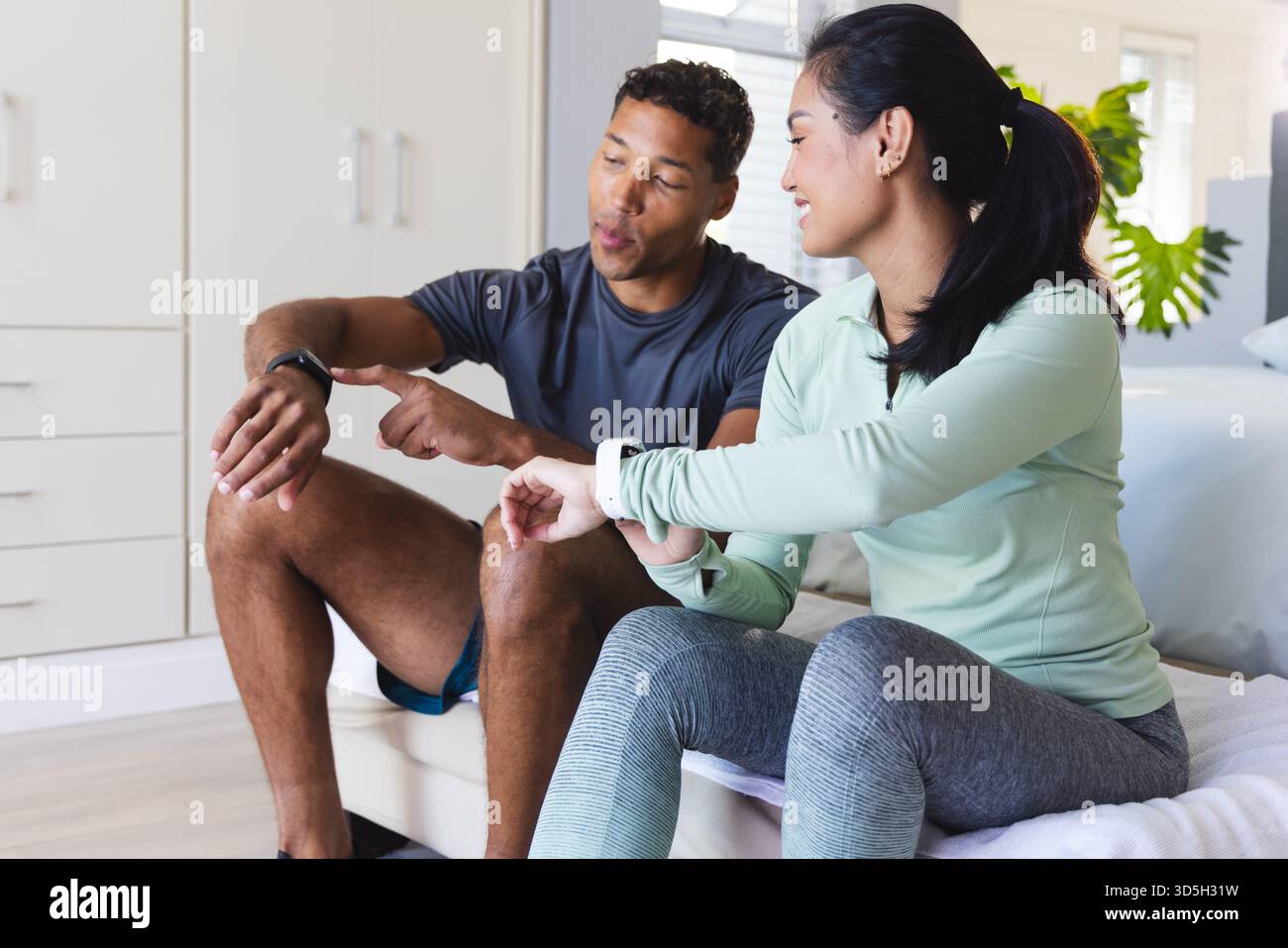Coppia a casa che controlla i tracker per il fitness, discutendo insieme i progressi dell'allenamento Foto Stock