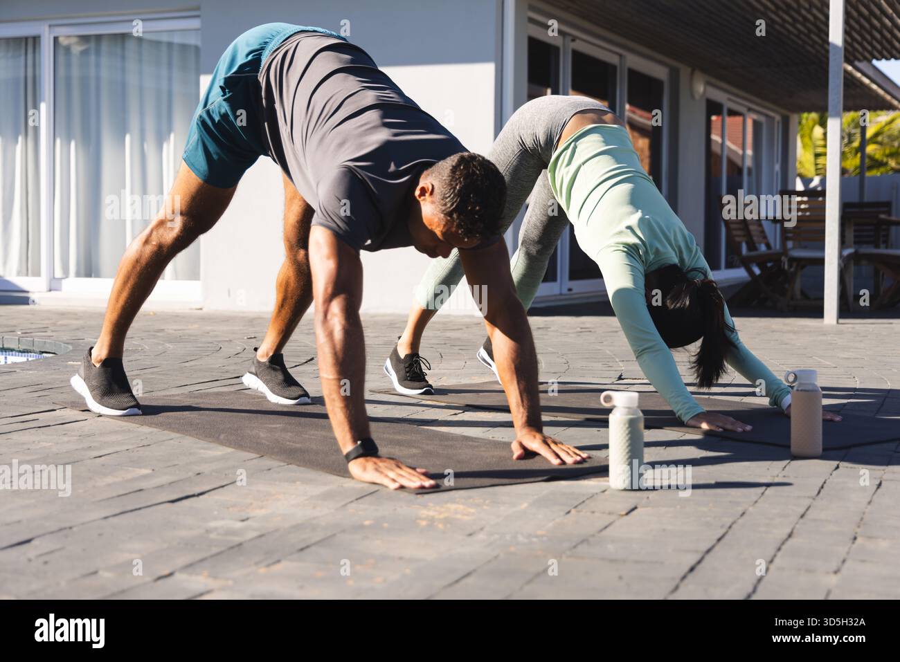 Coppia che pratica yoga all'aperto su tappeti, concentrandosi sulla posa verso il basso del cane Foto Stock