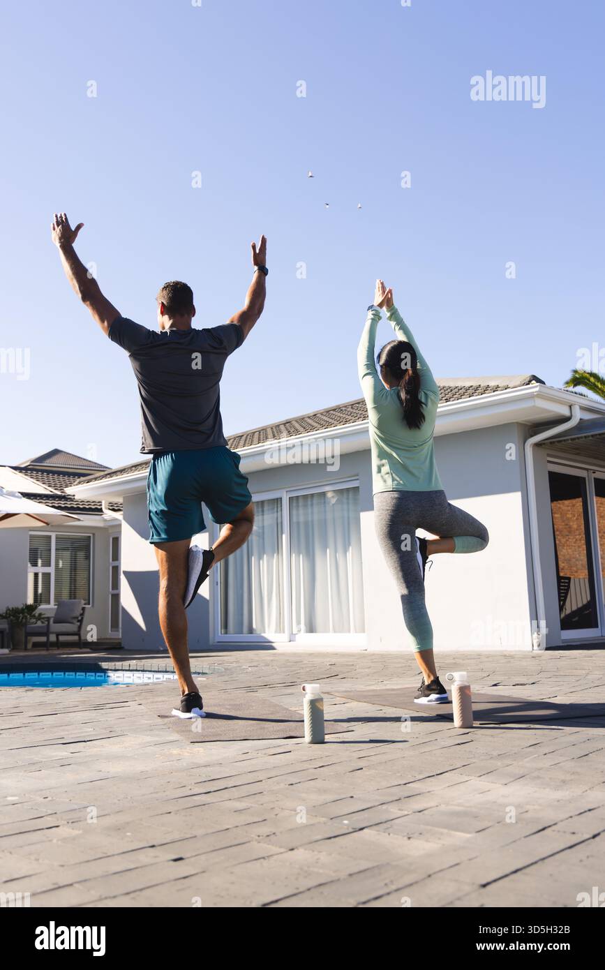 Coppia che pratica yoga all'aperto, bilanciandosi su una gamba vicino alla piscina Foto Stock