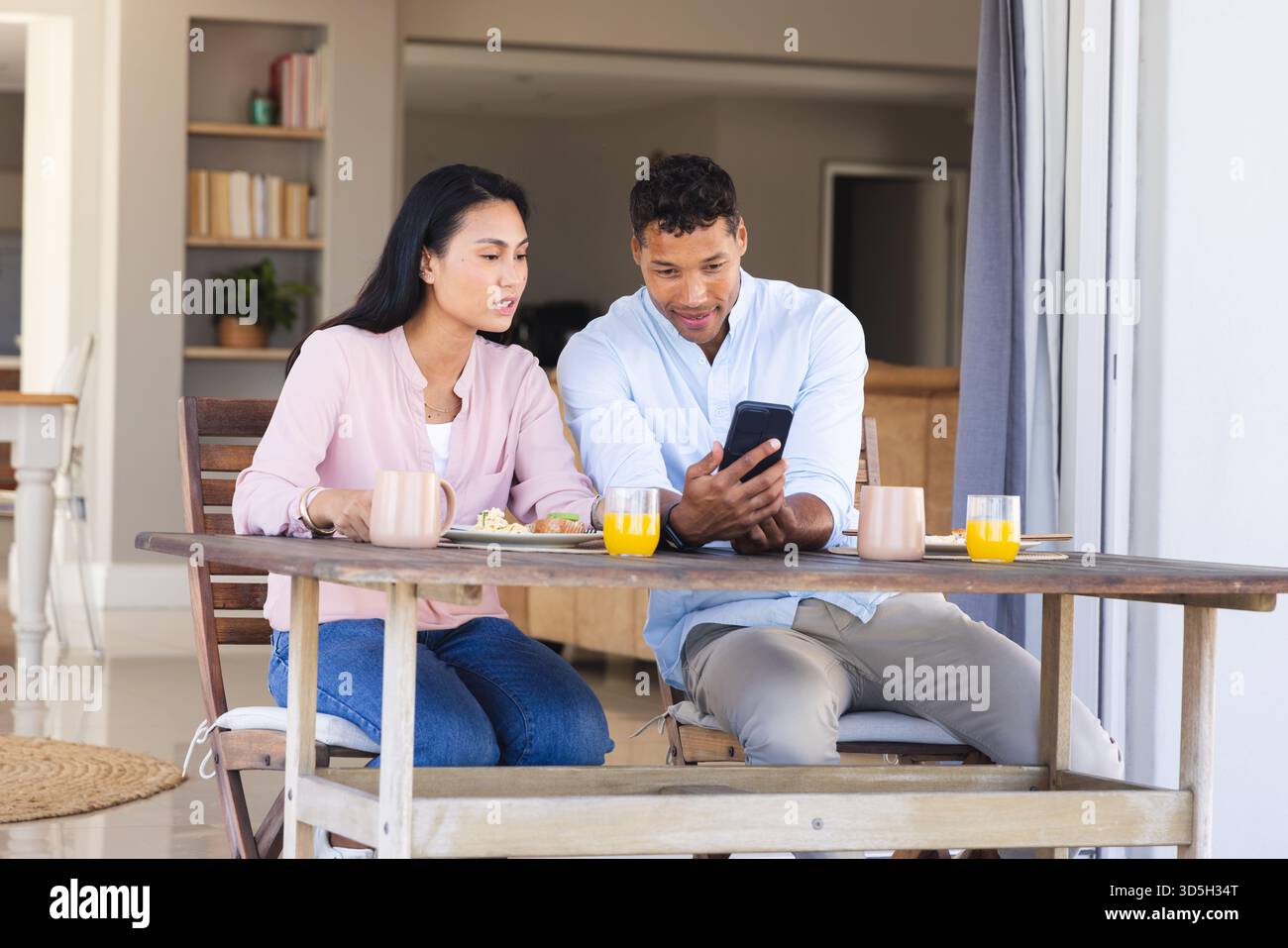 Coppia che fa colazione sul patio guardando insieme lo smartphone Foto Stock
