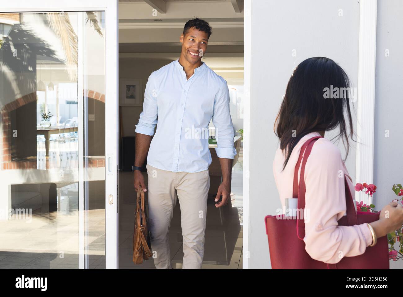 Coppia che si allunga all'ingresso di casa con piante e porta aperta, tenendo le borse e sorridendo Foto Stock