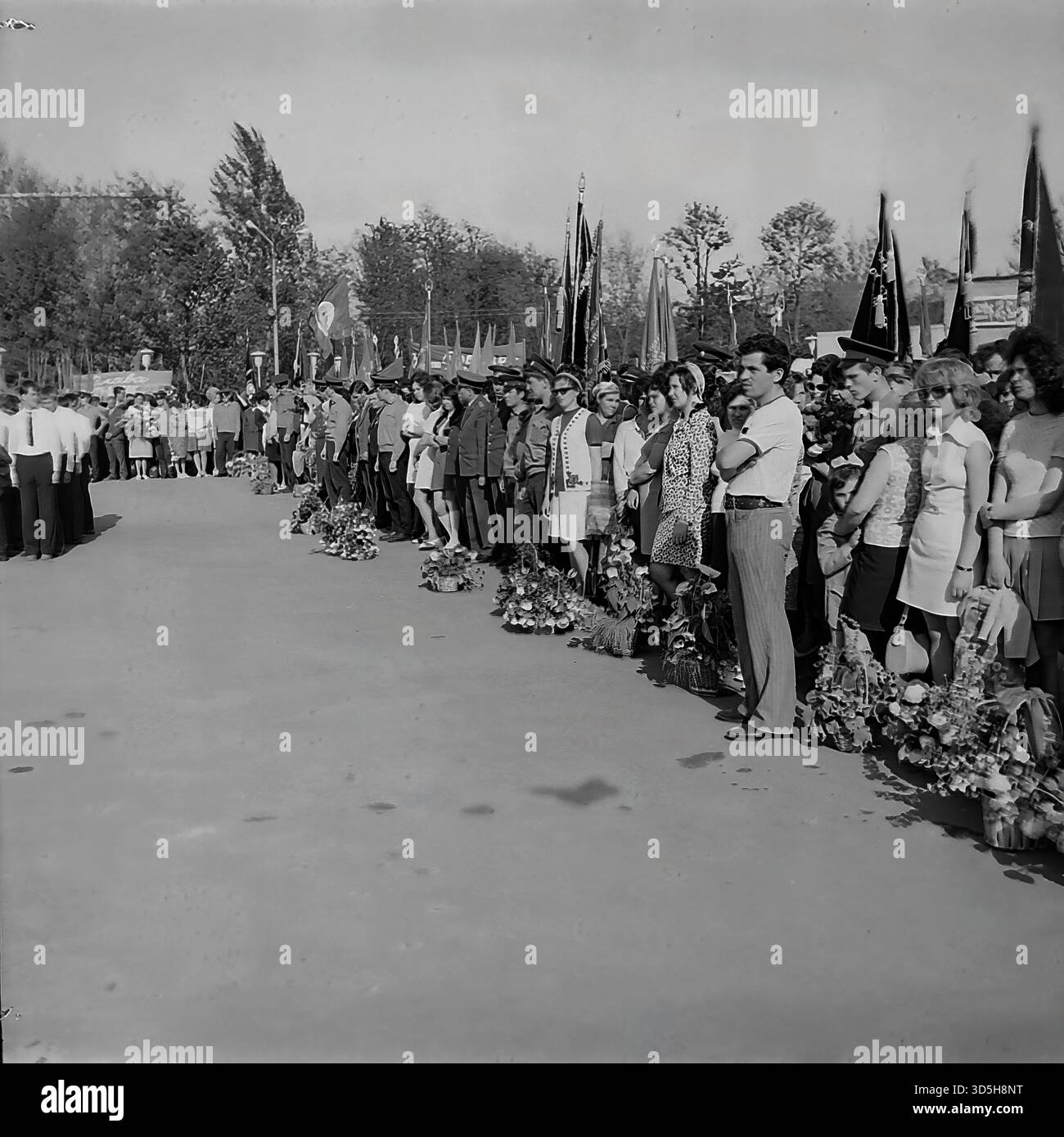 URSS, RSS Ucraina, Slavyansk, 1975. Un solenne raduno pubblico a Lenin Park (ora Shekovichny Park) per il 30° anniversario della Vittoria. Una folla di cittadini, lavoratori e personale militare si allinea nel vicolo. In primo piano, numerosi fiori e corone sono deposti a terra, pronti per la cerimonia. Una guardia d'onore dei giovani pionieri è all'attenzione. Questa fotografia d'archivio in bianco e nero cattura una cerimonia commemorativa e la vita sovietica negli anni '1970 Foto Stock