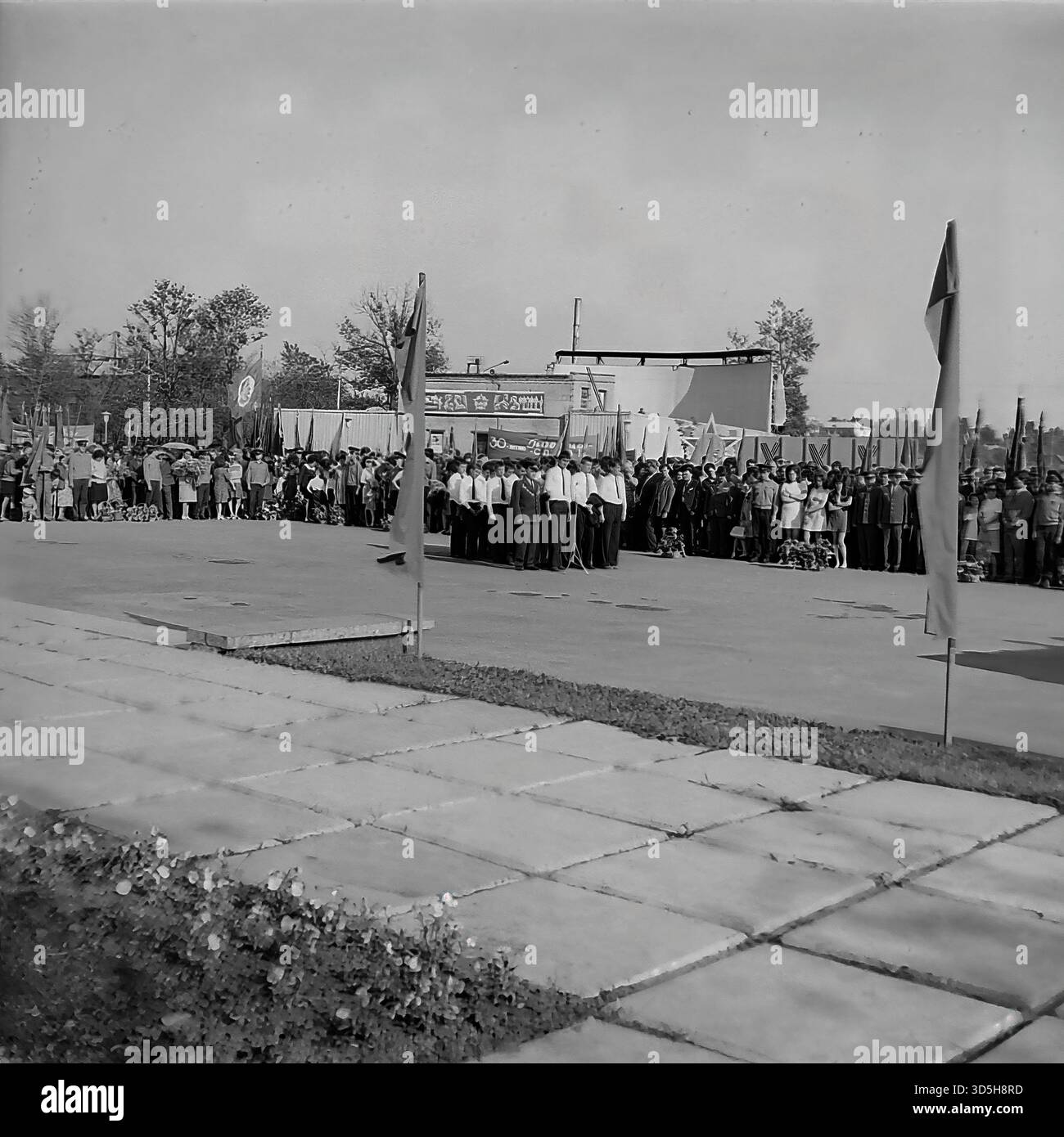 URSS, RSS Ucraina, Slavyansk, 1975. Un solenne raduno pubblico a Lenin Park (ora Shekovichny Park) per il 30° anniversario della Vittoria. Una folla di cittadini, lavoratori e personale militare si allinea nel vicolo. In primo piano, numerosi fiori e corone sono deposti a terra, pronti per la cerimonia. Una guardia d'onore dei giovani pionieri è all'attenzione. Questa fotografia d'archivio in bianco e nero cattura una cerimonia commemorativa e la vita sovietica negli anni '1970 Foto Stock