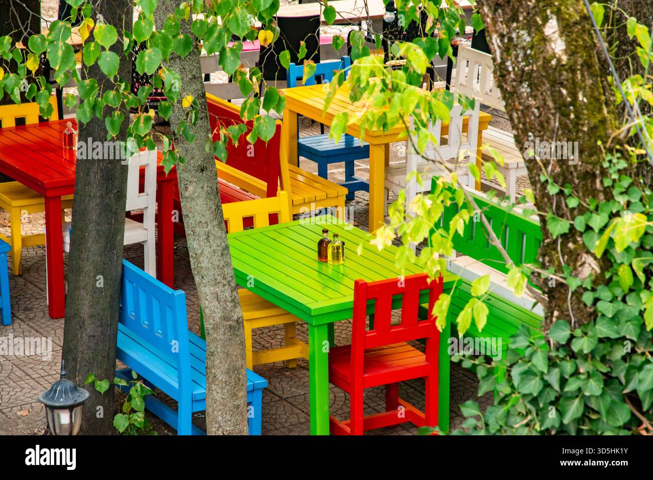 Vivaci tavoli e sedie in legno in un caffè all'aperto di campagna creano un'atmosfera rustica vivace, invitante e affascinante Foto Stock