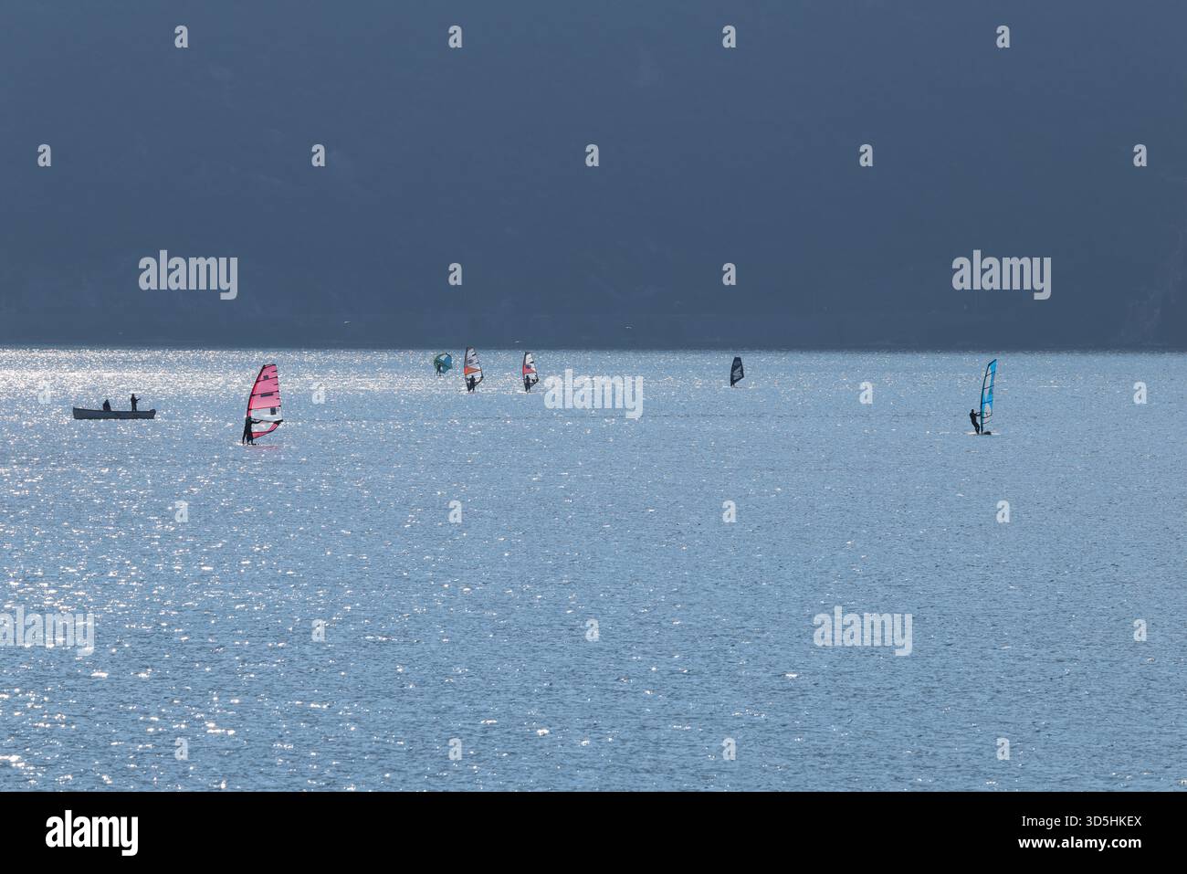 Gli amanti del windsurf scivolano in acque calme e scintillanti in una mattinata tranquilla sul Lago di Garda, in Italia Foto Stock