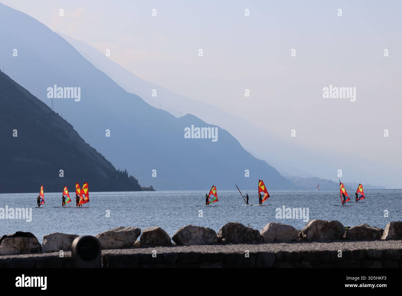 Allenamento scolastico di windsurf su un lago calmo con silhouette di montagna a strati sullo sfondo Foto Stock