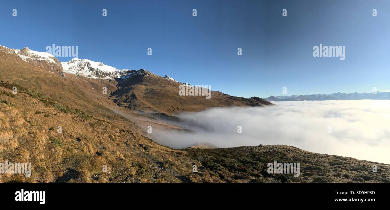 Paesaggio panoramico di fine autunno nelle Alpi svizzere Engadina, caratterizzato dalla nebbia mattutina che sale sulla valle e dai pendii di montagna dorati e illuminati dal sole, in Svizzera Foto Stock
